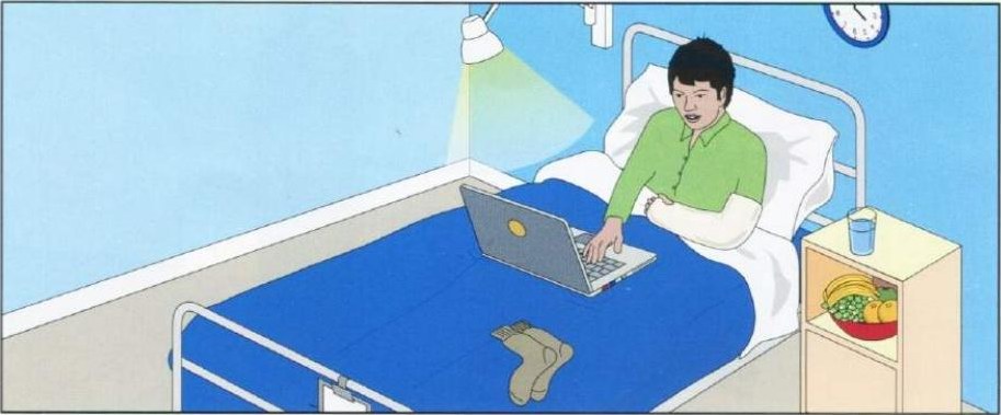 A boy in a green top sitting up in a hospital bed using a laptop, with one foot sticking out, a lamp above, a clock on the wall and a bowl of fruit and a glass on the bedside table.