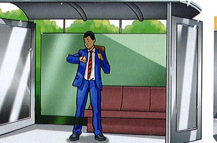 The boy waits at the bus stop and looks at his watch, worried